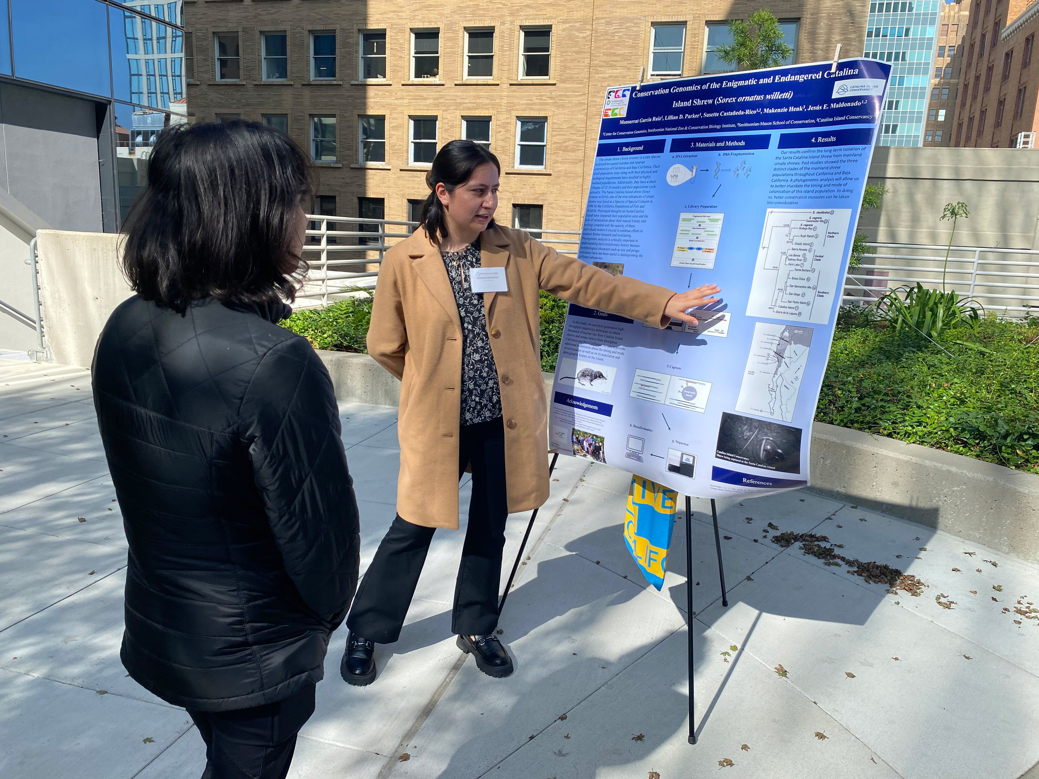 Photo of two people outside discussing a poster displayed on a tripod