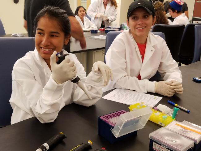 Two students in lab coats working with micropipettes