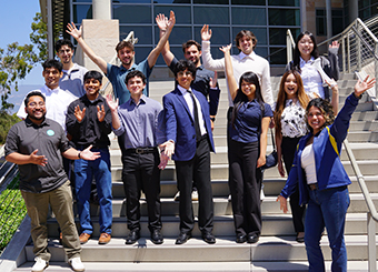 Thirteen people posing on stairs with arms outstretched