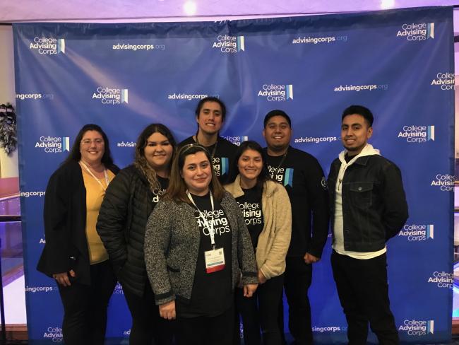 Group of seven people standing in front of a College Advising Corps background.