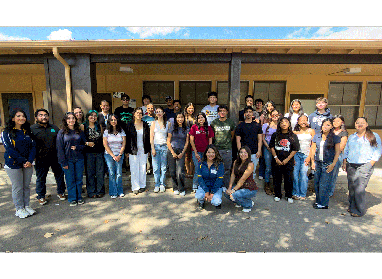 large group of people posed in front of a tan colored building