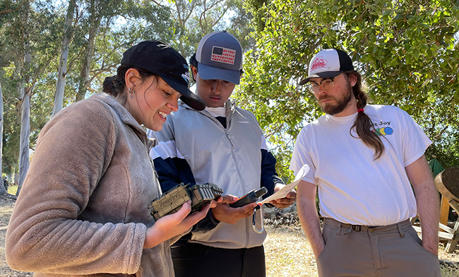 Photo of three people outside looking at a device in one person's hands